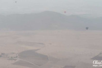Air balloons can be seen through low clouds as they rise above the desert.