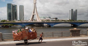 Man pulling a cart of trash across a large bridge. Man pulling a cart of trash across a large bridge.